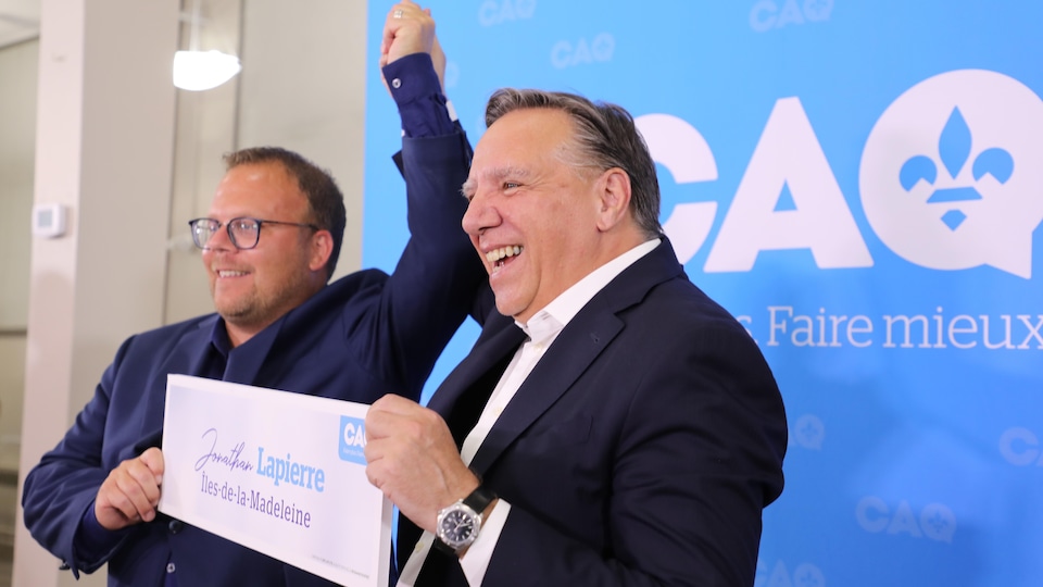 Jonathan Lapierre et François Legault, les mains dans les airs, devant une affiche de la CAQ lors de l'annonce.