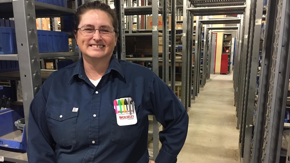 Une femme portant un uniforme de Wolseley Canada sourit à la caméra dans un entrepôt.