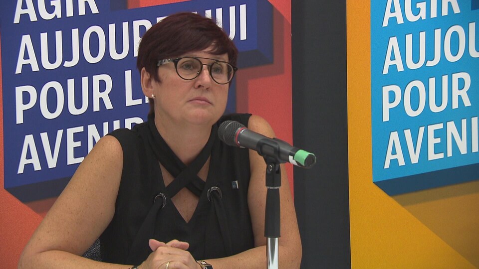 Josée Scalabrini assise à une table de presse devant un micro. 