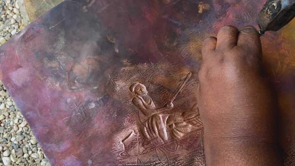 L'artiste Joséphine Tambwe Feza Kabibi travaille une oeuvre en cuivre martelé intitulée Voyage en pirogue. 