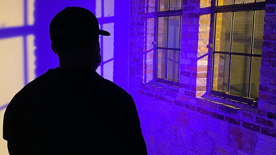 Un homme dont on distingue la silhouette dans une pièce sombre.