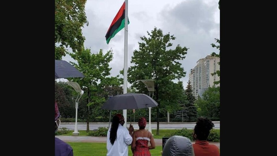 Des gens protégés par des parapluies regardent le drapeau monter.