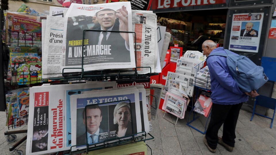 Un homme marche devant un kiosque à journaux où le résultat du premier tour à l'élection présidentielle française se retrouve en une.