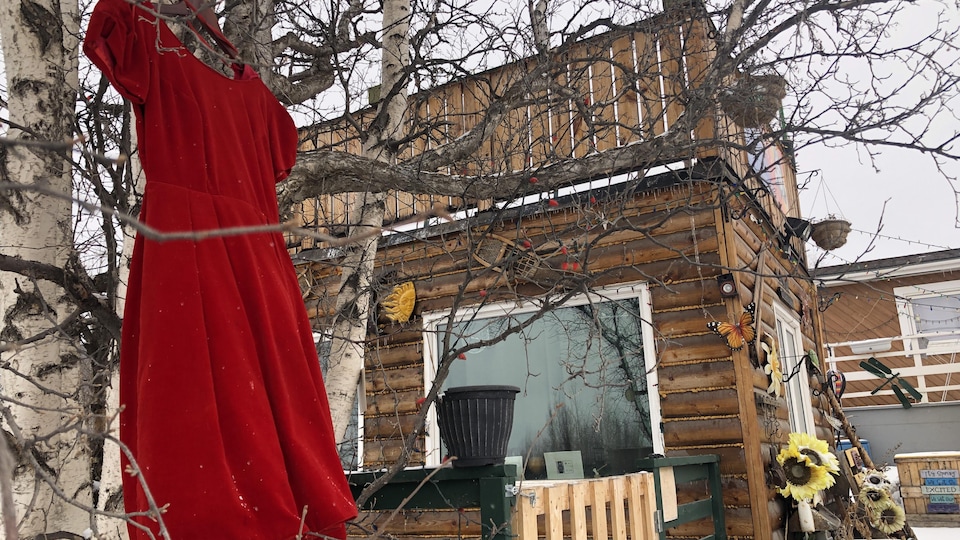 Une robe rouge pend à un arbre devant une maison en bois.