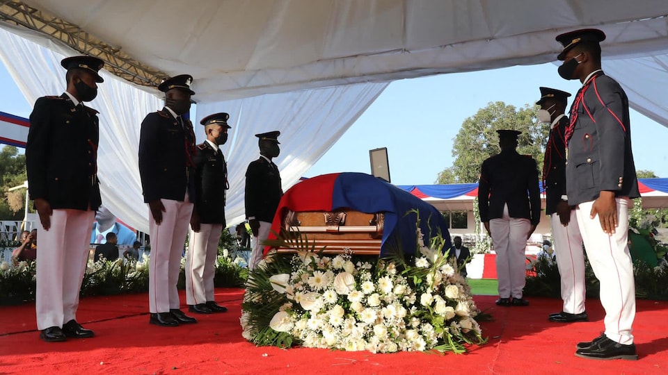 Des membres de la garde, en uniforme d'apparat, se tiennent devant un cercueil recouvert du drapeau haïtien. 