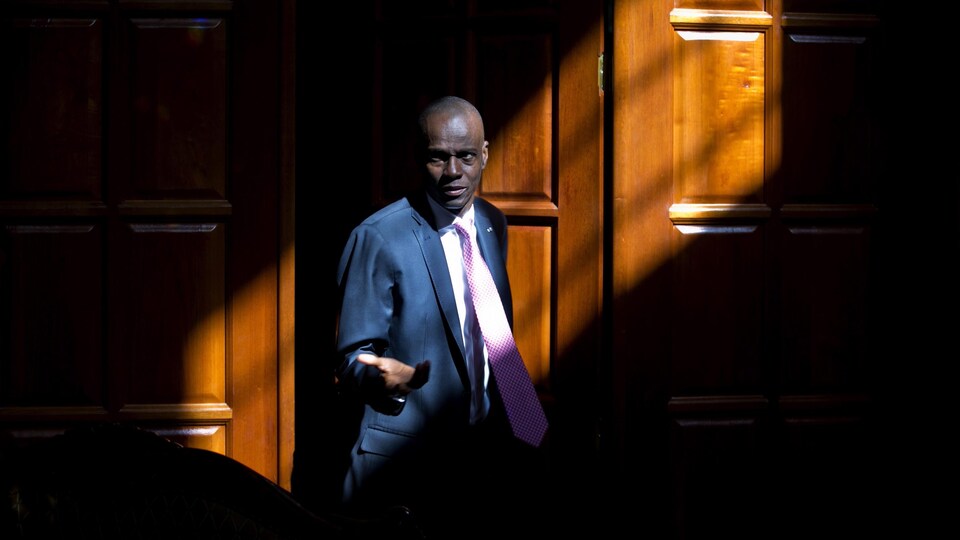 Jovenel Moïse photographié devant une porte dans un rayon de lumière.