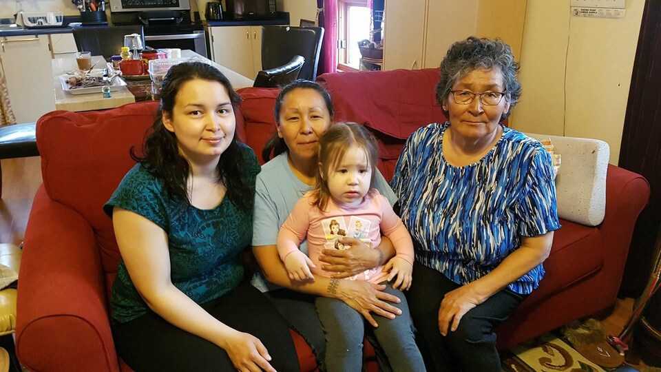 Trois femmes et une petite assises sur un divan rouge.