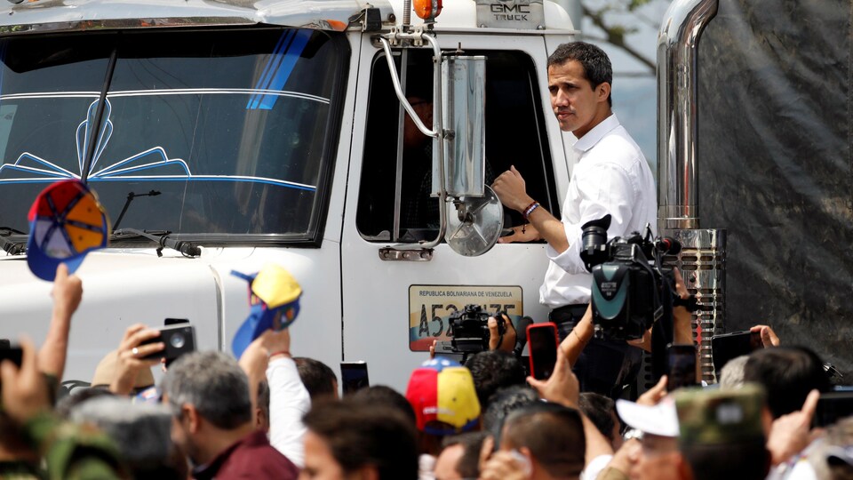 Juan Guaido se tient debout sur un camion de livraison entouré par une foule de gens. 