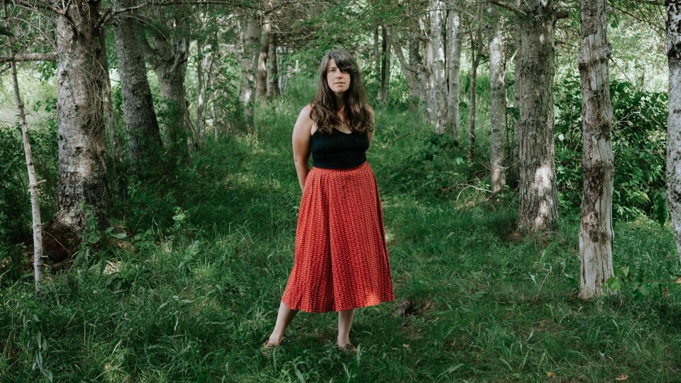 La femme se tient au milieu d'une rangée d'arbres.