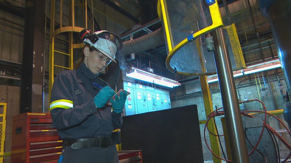 Une femme écrit sur un calepin à l'intérieur d'une usine.