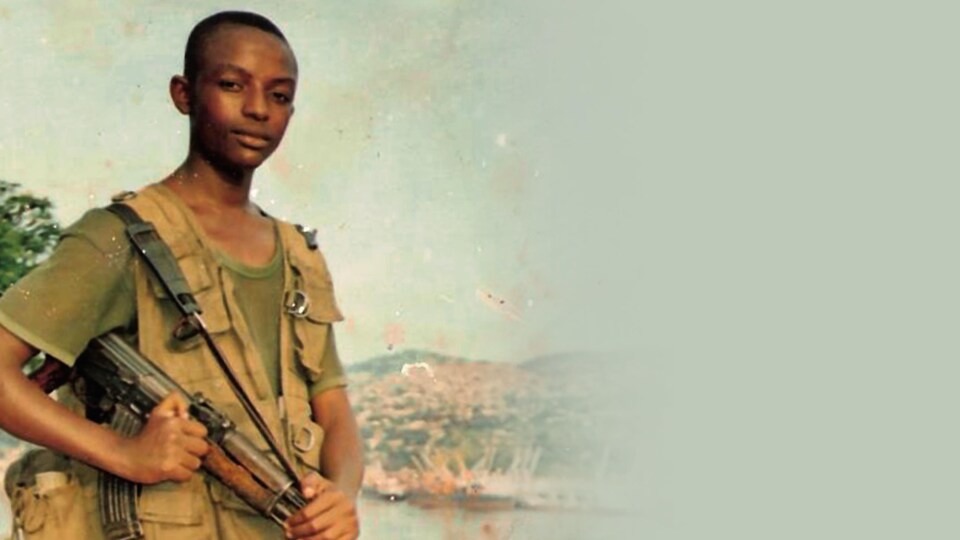 Junior Nzita en tenue militaire tient une arme en main.
