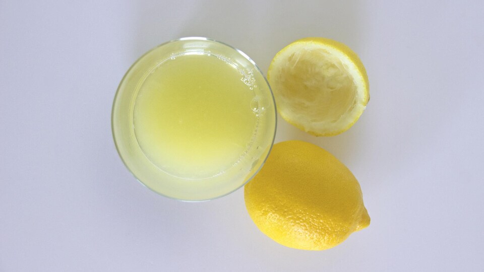 Un verre de jus de citron et un citron pressé.