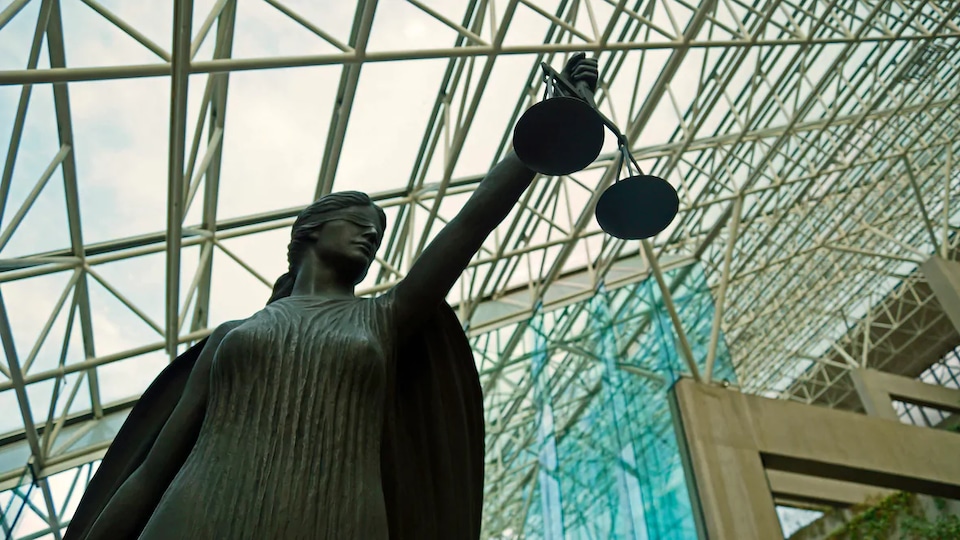 Une statue aux yeux bandés tient une balance sous le toit en verre du palais de justice à Vancouver.