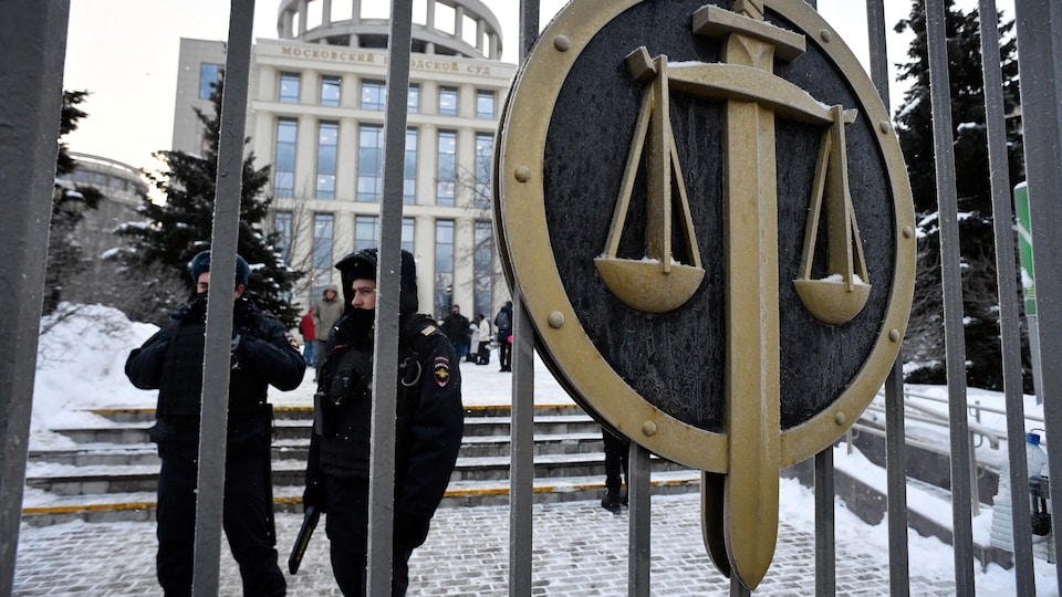 Des policiers, derrière une grille, portent le symbole de la justice.