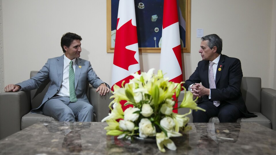 Deux hommes discutent devant des drapeaux canadiens. 