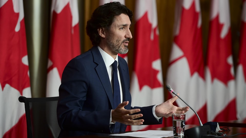 Justin Trudeau en conférence de presse devant des drapeaux du Canada.