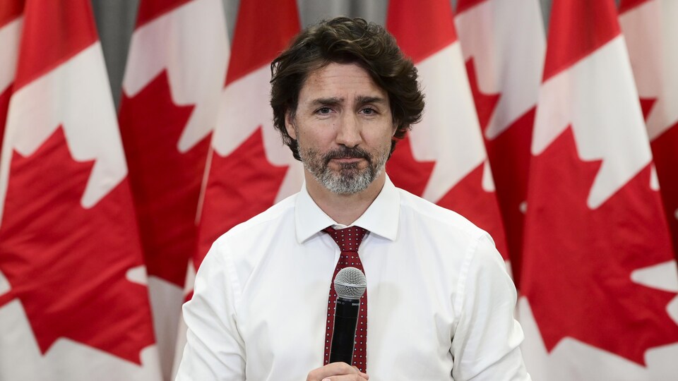 Justin Trudeau, in the microphone, in front of the flags of Canada.