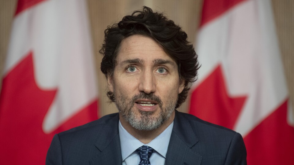 Le premier ministre est assis devant des drapeaux du Canada.
