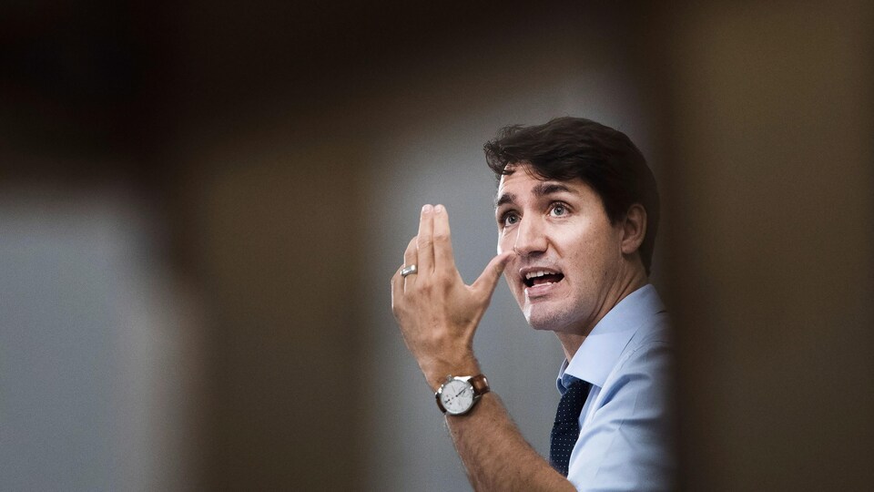 Gros plan de Justin Trudeau qui lève la main gauche en regardant au loin.