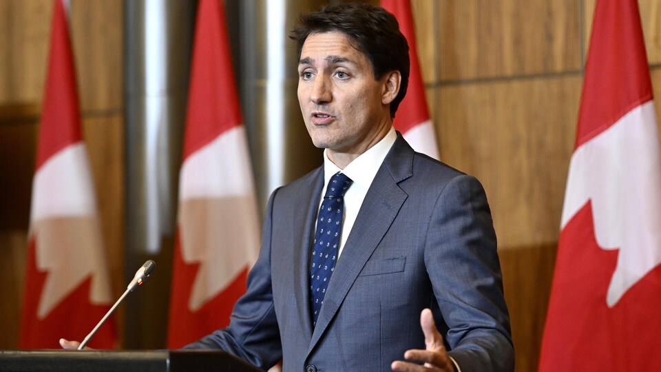 Justin Trudeau devant un micro et une tribune, s'adresse à ses interlocuteurs. 