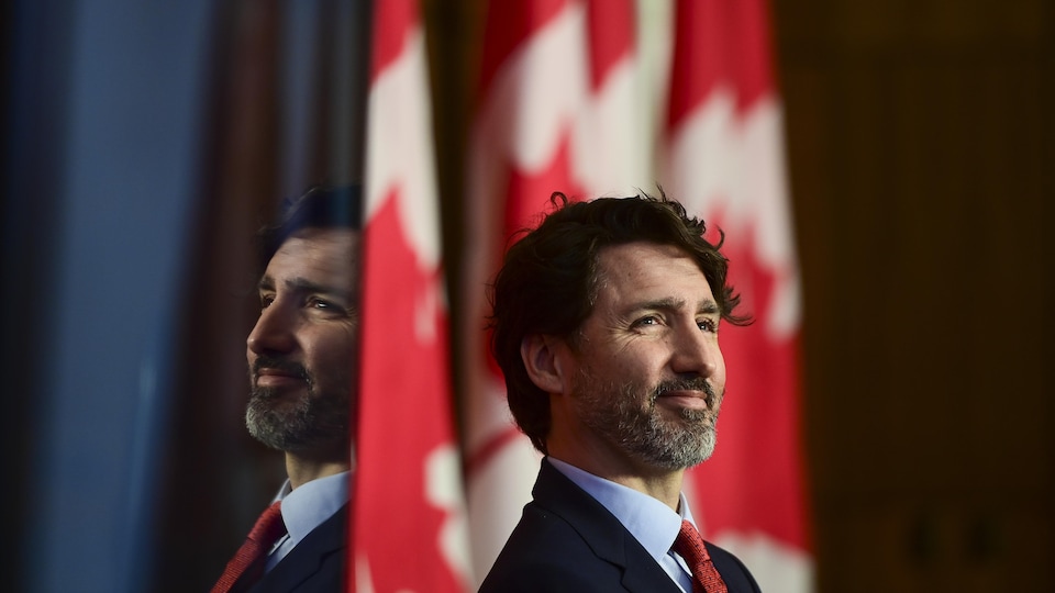 Justin Trudeau souriant devant un drapeau du Canada.