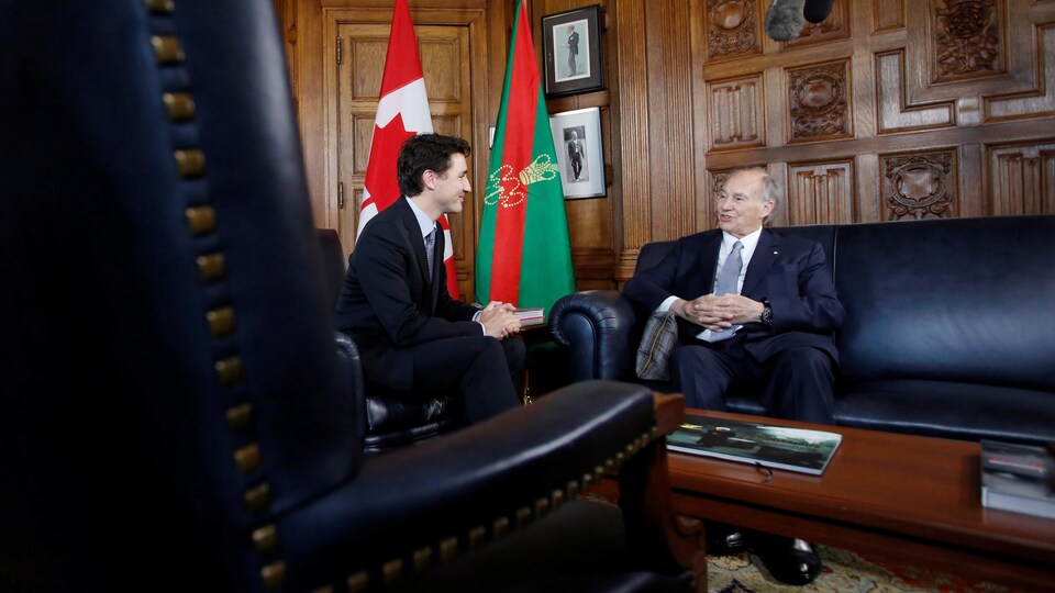 Les deux hommes sont assis de biais sur de magnifiques divans dans un bâtiment du parlement canadien.