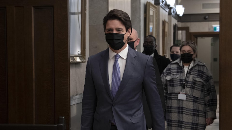 Justin Trudeau, le visage masqué, marche dans un corridor suivi de quelques personnes, masquées elles aussi.