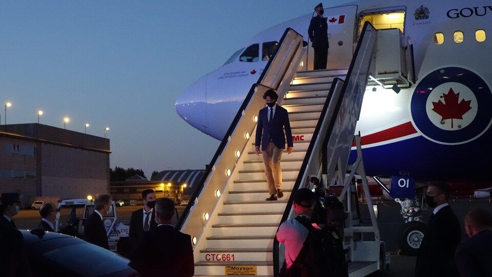 Justin Trudeau descend, masqué, l'escalier de l'avion du gouvernement canadien à la nuit tombante.