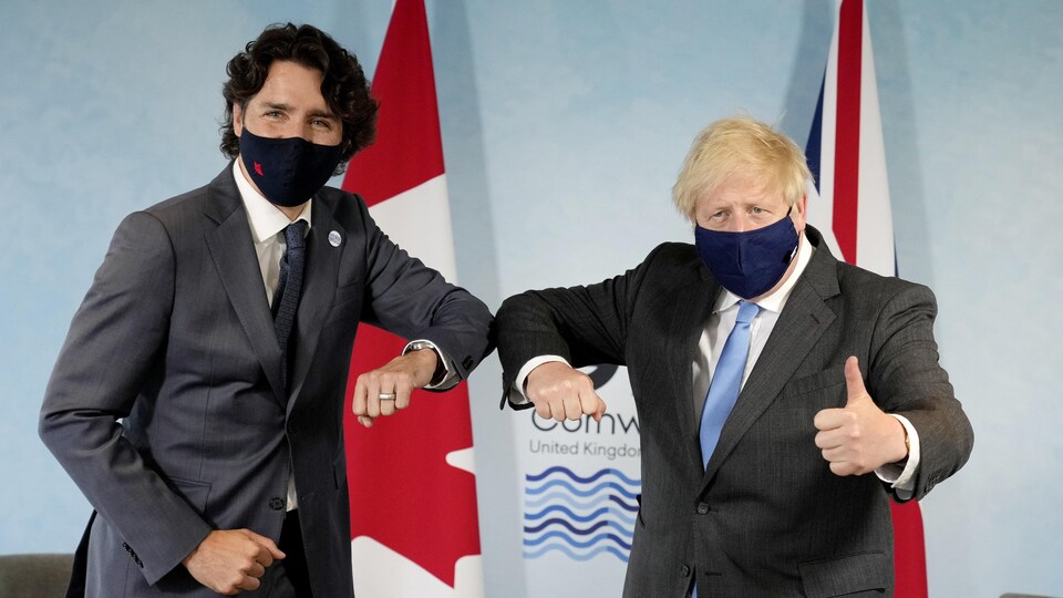 Deux hommes masqués devant un drapeau du Canada et un drapeau du Royaume-Uni posent pour la caméra.