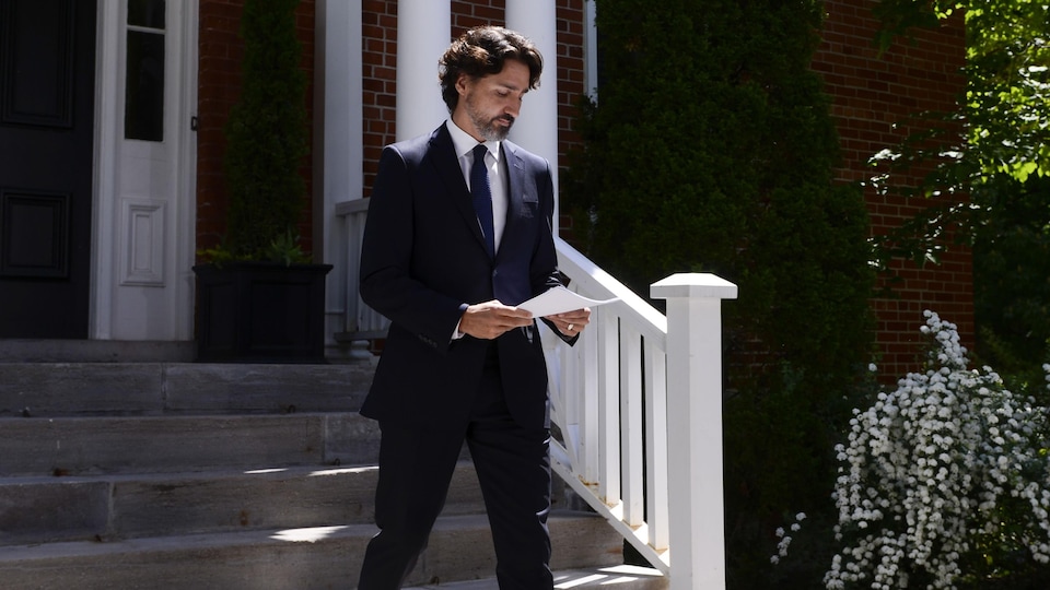 Justin Trudeau sort de sa maison en tenant des feuilles de papier.
