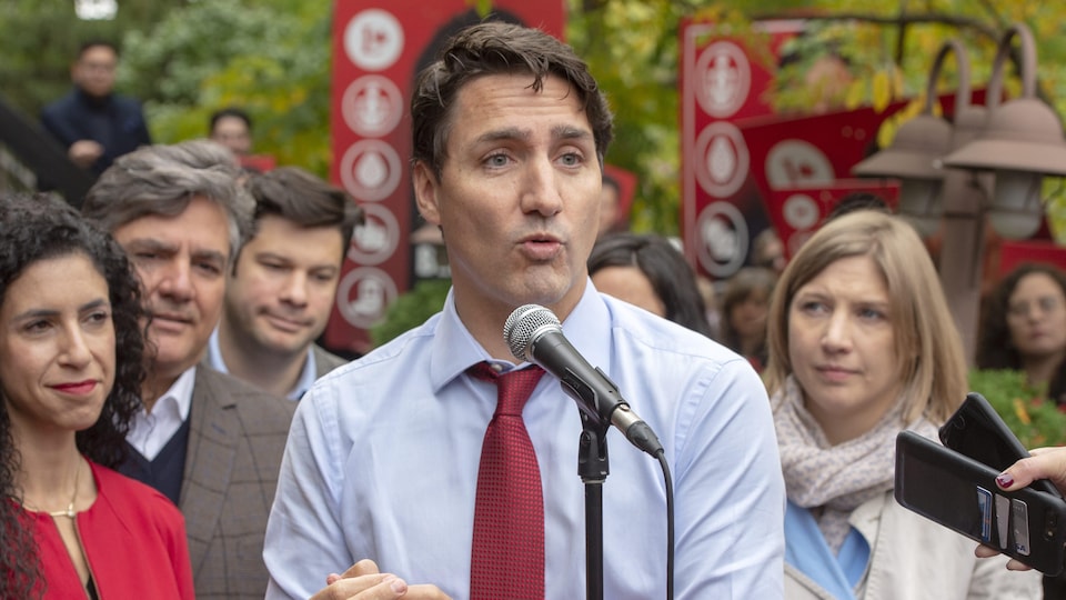 Justin Trudeau parle devant un micro, entouré des gens, dans un parc.