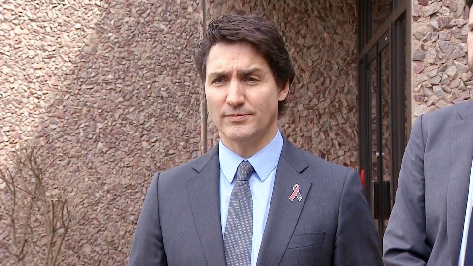 Justin Trudeau debout à l'extérieur, l'air sérieux, devant un édifice de pierre.