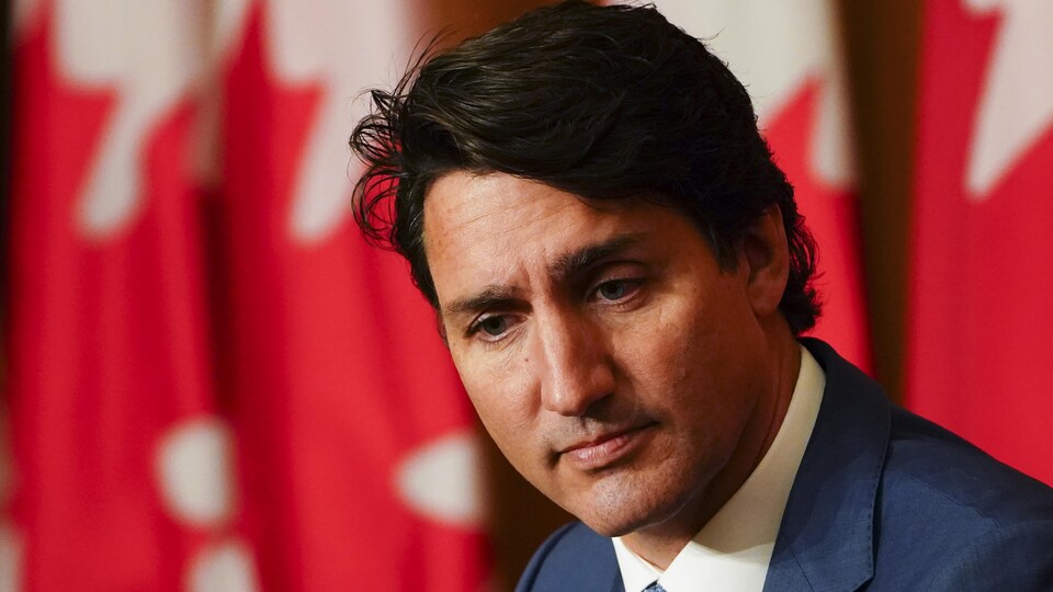 Plan rapproché de Justin Trudeau en conférence de presse, sur fond de drapeaux canadiens.