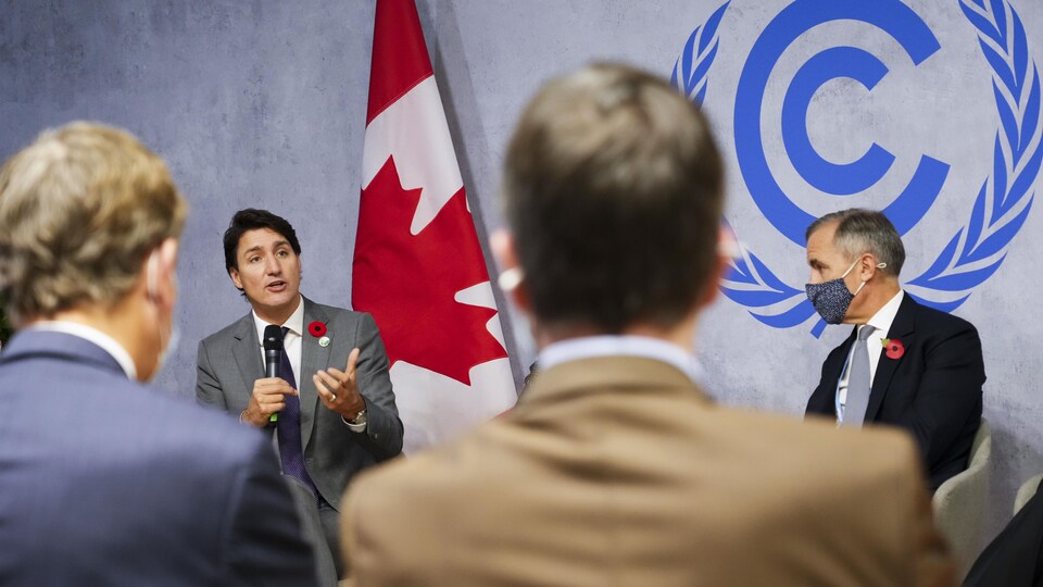 Justin Trudeau parle dans un micro, des personnes qui l'entourent l'écoutent.