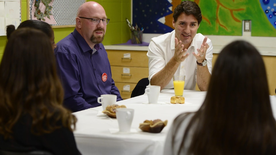 Justin Trudeau parle à une enseignante assise avec des collègues autour d'une table.