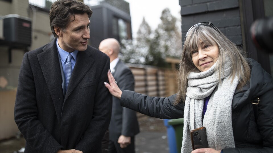 Une femme met sa main sur l'épaule de Justin Trudeau, sans le regarder, tandis qu'il tente de lui parler.