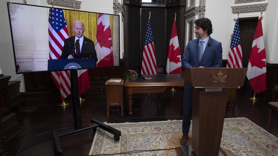 Justin Trudeau regarde Joe Biden, sur un écran, en souriant.