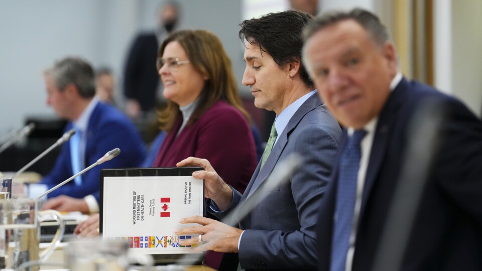 Le premier ministre Justin Trudeau ouvre un livre d'information intitulé « Réunion de travail des premiers ministres sur les soins de santé » alors qu'il rencontre les premiers ministres du Canada à Ottawa le mardi 7 février 2023. La première ministre du Manitoba, Heather Stefanson, est assise à sa droite, et le premier ministre du Québec, François Legault, à sa gauche.