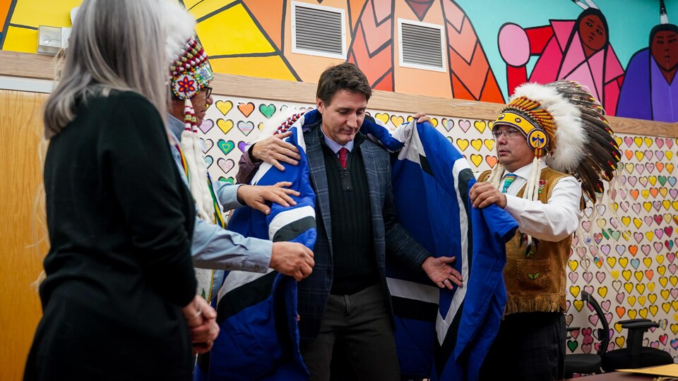 Le premier ministre du Canada, Justin Trudeau, reçoit une couverture de la part du chef de la Première Nation Chakastaypasin, Calvin Sanderson, (à gauche) et du chef de la Nation crie James Smith, Wally Burns, (à droite) lors d'une visite dans la Nation crie le 28 novembre 2022.