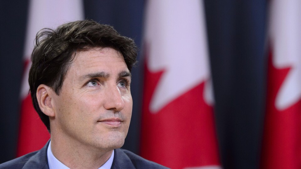 Justin Trudeau en conférence de presse, devant des drapeaux du Canada.
