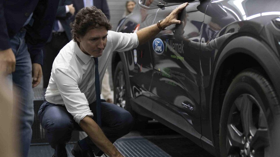 Justin Trudeau s'accroupit pour examiner une voiture.