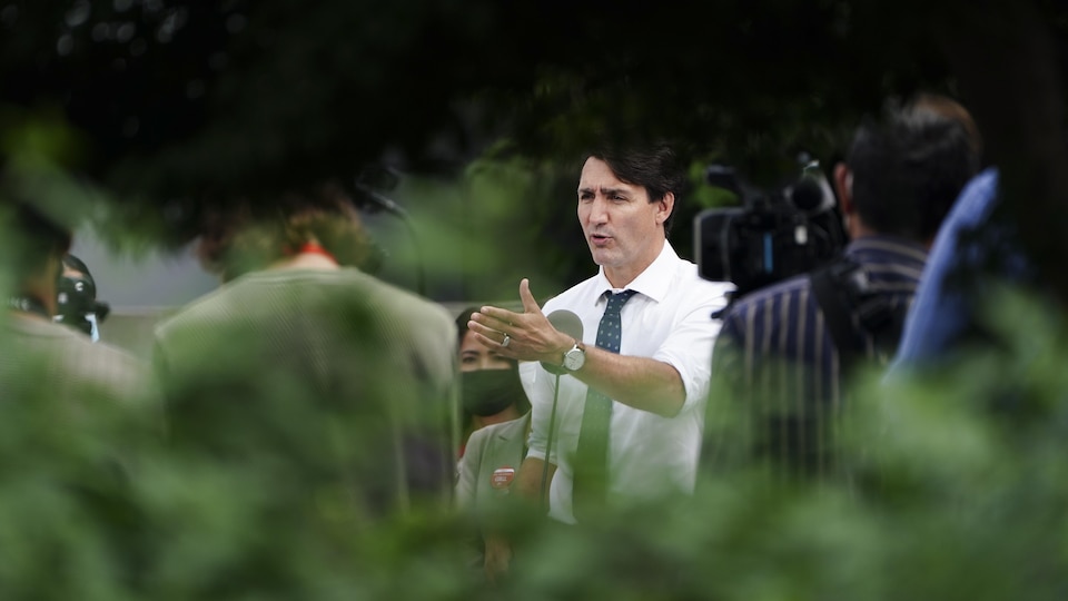 Justin Trudeau, vu à travers les feuilles d'arbres, lors d'un point de presse.