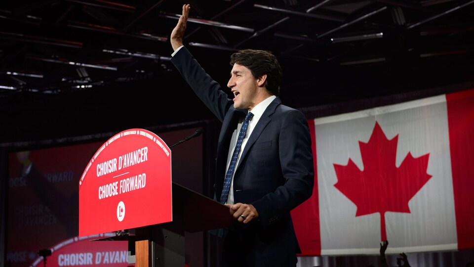 Justin Trudeau, sur scène, salue la foule en souriant.