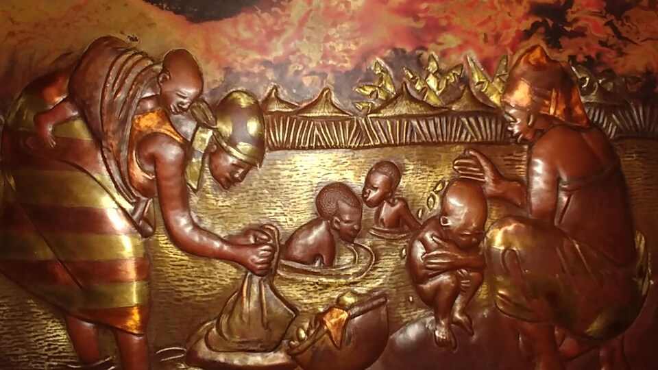 Un plaque de cuivre sur laquelle se dessine en relief un scène où des femmes et des enfants se baignent dans une rivière. Une femme nettoie du linge avec un bébé attaché dans le dos, une autre femme lave un enfant.