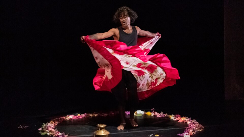 Une artiste danse avec une jupe rose avec des pétales de fleurs sur le sol. 