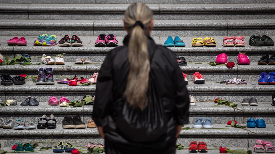 Une femme, de dos, regardant les chaussures d'enfants alignées sur des marches.