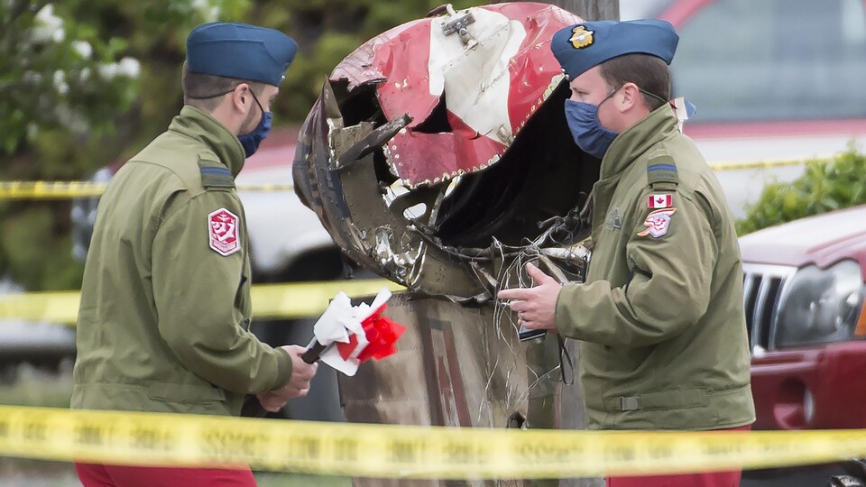 Deux membres des forces armées en uniforme sevant un débris d'avion.