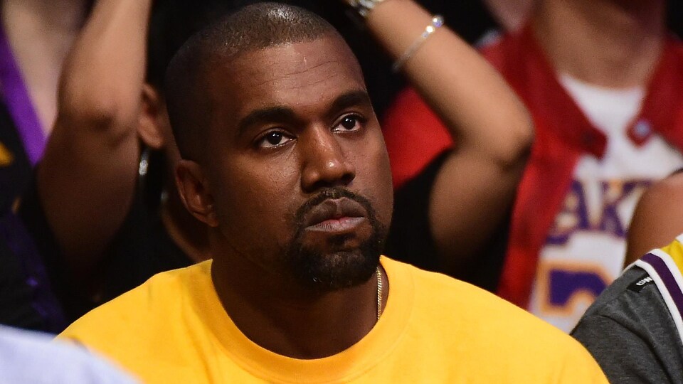 Le visage fermé, le chanteur américain Kanye West regarde un match de basketball.