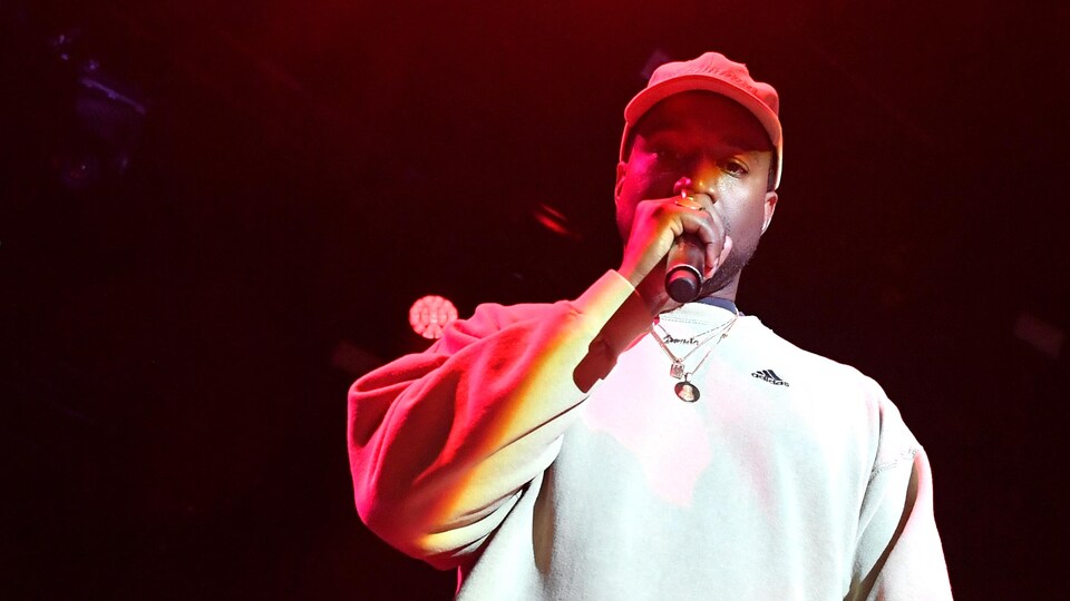 Kanye West avec un micro à la main sur scène lors d'un événement promotionnel.