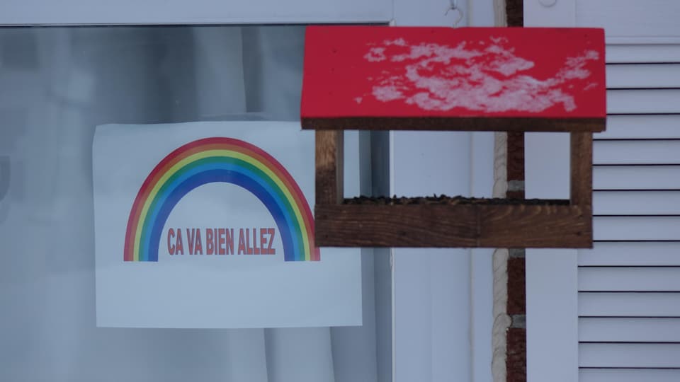 Une affiche avec un arc-en-ciel et une cabane d’oiseaux devant une fenêtre